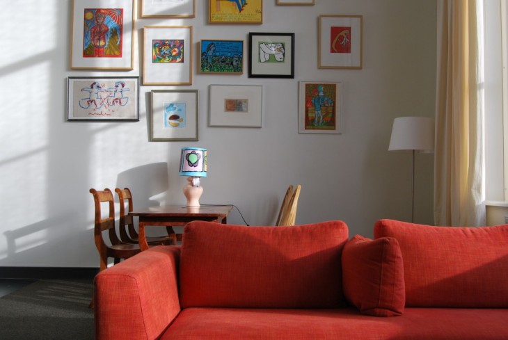 sfeerbeeld van een familiekamer met in beeld een oranje bank, een eettafel met 4 stoelen en op de muur diverse schilderijen